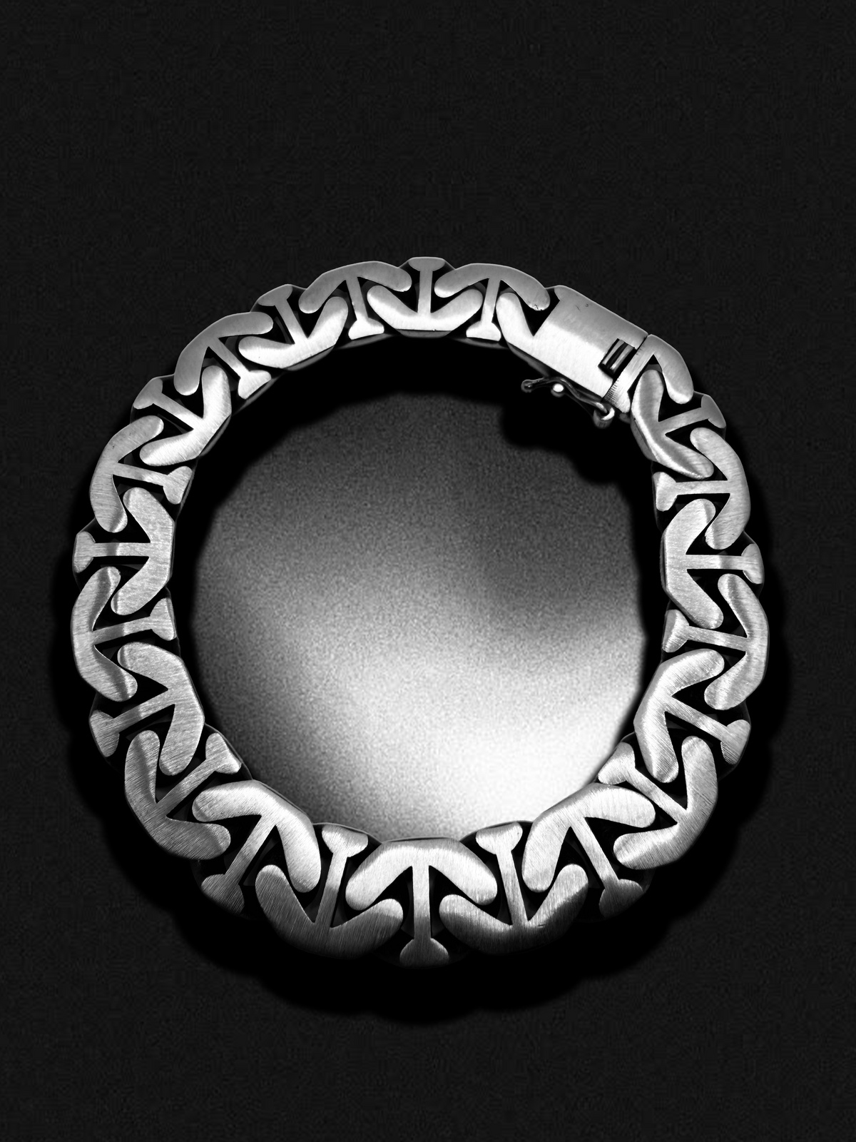 Nocturne Lock Bracelet laid in a circle on black, showing the brushed mariner links and the box clasp